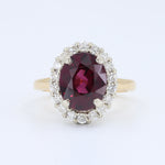 Load image into Gallery viewer, Gold halo ring featuring an oval red ruby center stone surrounded by sparkling white diamonds.