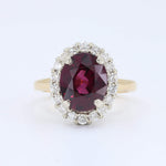 Load image into Gallery viewer, Gold halo ring featuring an oval red ruby center stone surrounded by sparkling white diamonds. Elegant and luxurious.