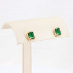Load image into Gallery viewer, Emerald green square stud earrings with gold-tone bezel setting on a soft display stand.