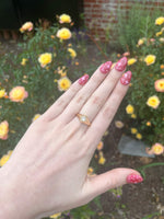 Load image into Gallery viewer, Gold geometric ring with a sparkling clear stone, worn on a hand with bright pink glitter nails among yellow roses.