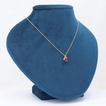 Load image into Gallery viewer, Gold chain necklace featuring a delicate red gemstone pendant, displayed on a blue velvet bust.