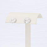 Load image into Gallery viewer, Silver flower stud earrings with a textured finish, stylishly displayed on a cream-colored earring holder.