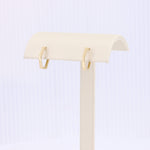 Load image into Gallery viewer, Gold geometric hoop earrings displayed on a soft cream-colored stand. Modern, minimalist style in shining metal.