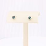 Load image into Gallery viewer, A pair of elegant teal crystal stud earrings in gold settings on a cream display stand.