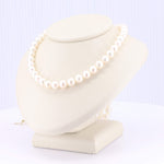 Load image into Gallery viewer, Elegant white pearl necklace on cream-colored display, featuring lustrous, round freshwater pearls for a classic style.