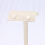 Load image into Gallery viewer, Delicate white pearl stud earrings displayed on a cream velvet stand, perfect for elegant occasions.