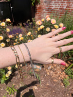 Load image into Gallery viewer, Stylish gold and silver chain bracelets on a hand, set against a vibrant floral garden background.