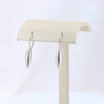 Load image into Gallery viewer, Sleek silver drop earrings in a modern, minimalist design on a display stand.