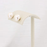 Load image into Gallery viewer, Classic white pearl stud earrings displayed on a minimalist cream stand, perfect for any elegant occasion.
