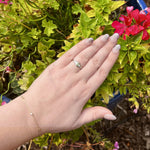 Load image into Gallery viewer, Sterling silver ring with green gemstone, worn on a hand amidst vibrant green foliage and pink flowers.