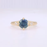 Load image into Gallery viewer, Gold ring featuring a round, teal sapphire center stone and two sparkling diamond accents. Elegant and timeless design.