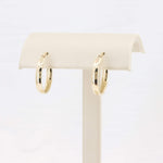 Load image into Gallery viewer, Gold hoop earrings on a cream display stand, featuring a sleek, modern design crafted from polished metal.