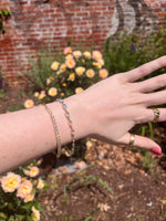 Load image into Gallery viewer, Gold chain bracelet with clear crystals, stylishly worn on a hand amidst a floral garden background.