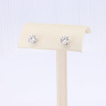 Load image into Gallery viewer, Silver-tone round cubic zirconia stud earrings on a beige display stand. Elegant and timeless for any occasion.