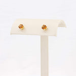 Load image into Gallery viewer, Gold stud earrings with amber-colored stones on a cream display stand. Elegant, modern jewelry accessory.