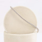 Load image into Gallery viewer, Silver tennis bracelet adorned with round brilliant-cut diamonds, elegantly displayed on a soft cream-colored pedestal.