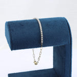 Load image into Gallery viewer, Gold-tone bracelet with sparkling clear crystals on a soft blue display stand. Elegant and stylish for any occasion.