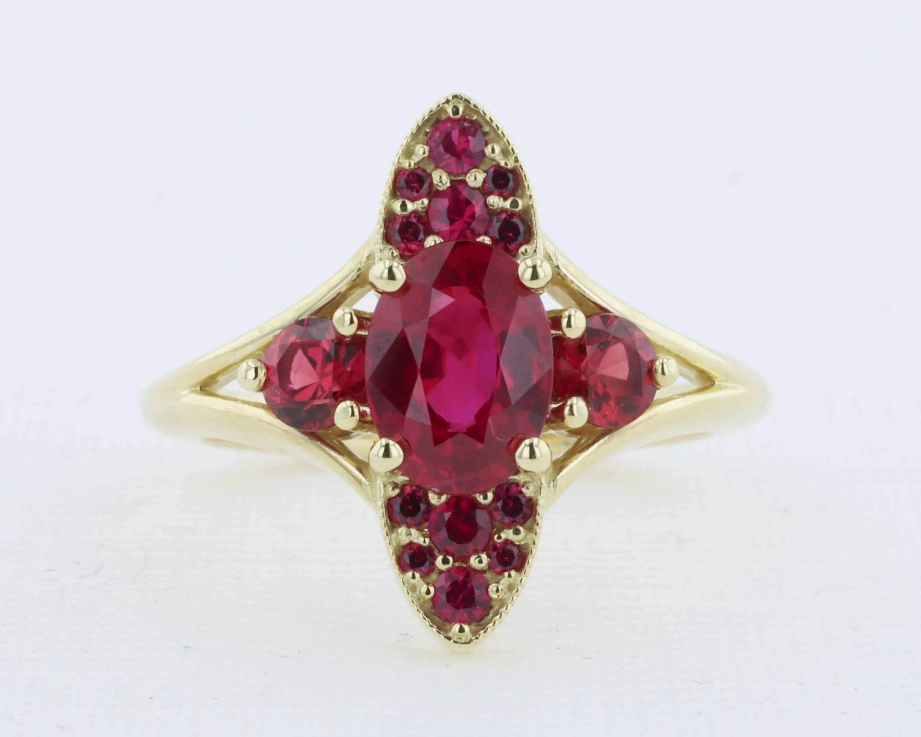 Gold ring featuring an oval red ruby centerpiece and round red gemstones in a vintage floral design.
