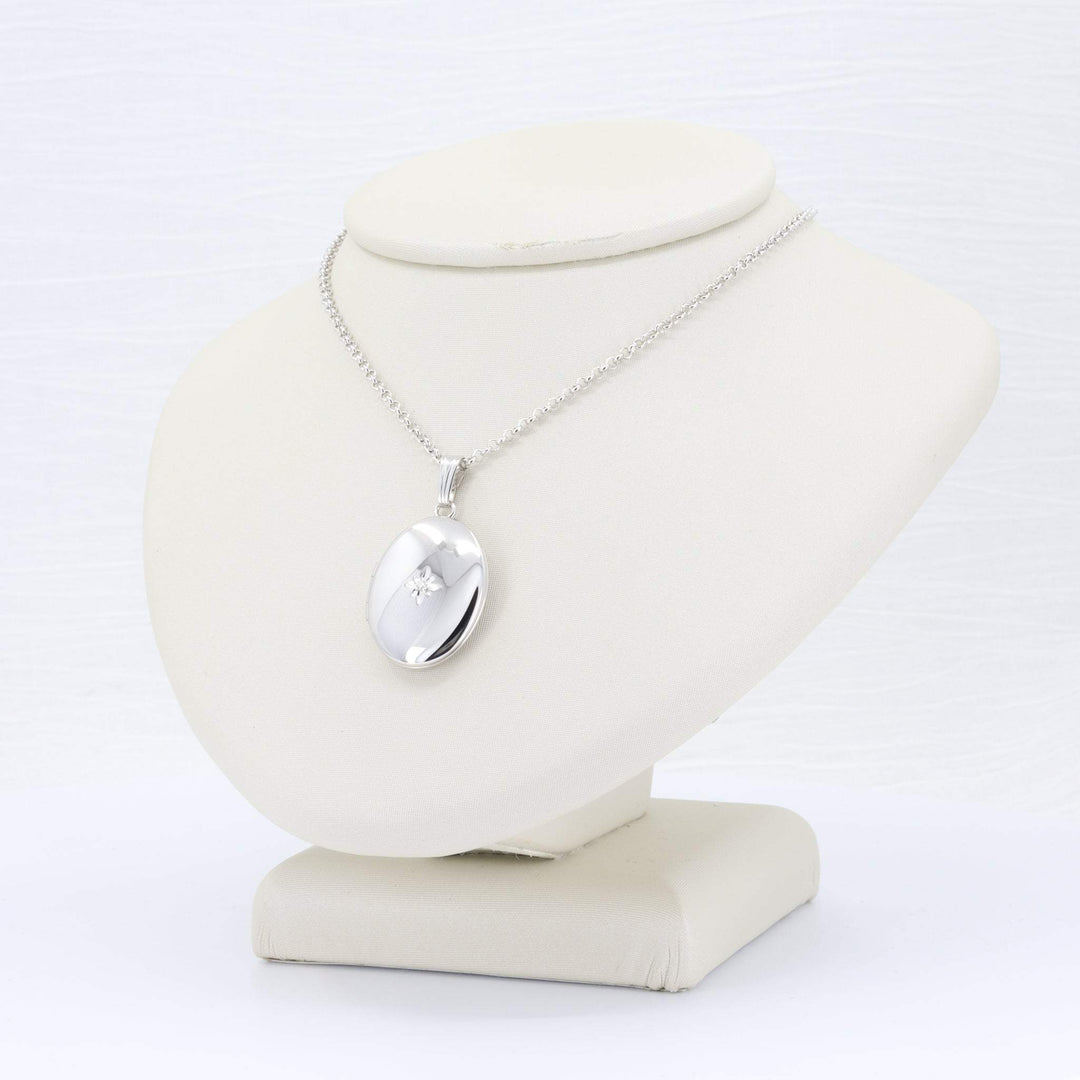 Silver oval locket necklace with diamond accent on a delicate chain, displayed elegantly on a neutral-colored bust.