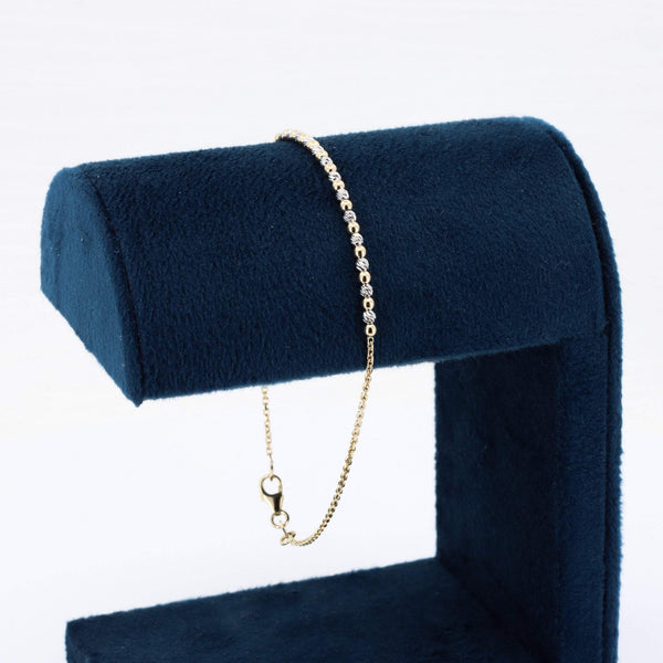 Gold chain bracelet with shimmering beads, displayed on a navy blue velvet stand.