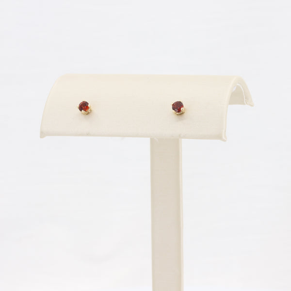 Gold stud earrings with red gemstones, elegantly displayed on a cream-colored jewelry stand.