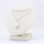 Load image into Gallery viewer, Silver floral locket pendant necklace on a sleek display stand, featuring intricate detailing and a sparkling chain.