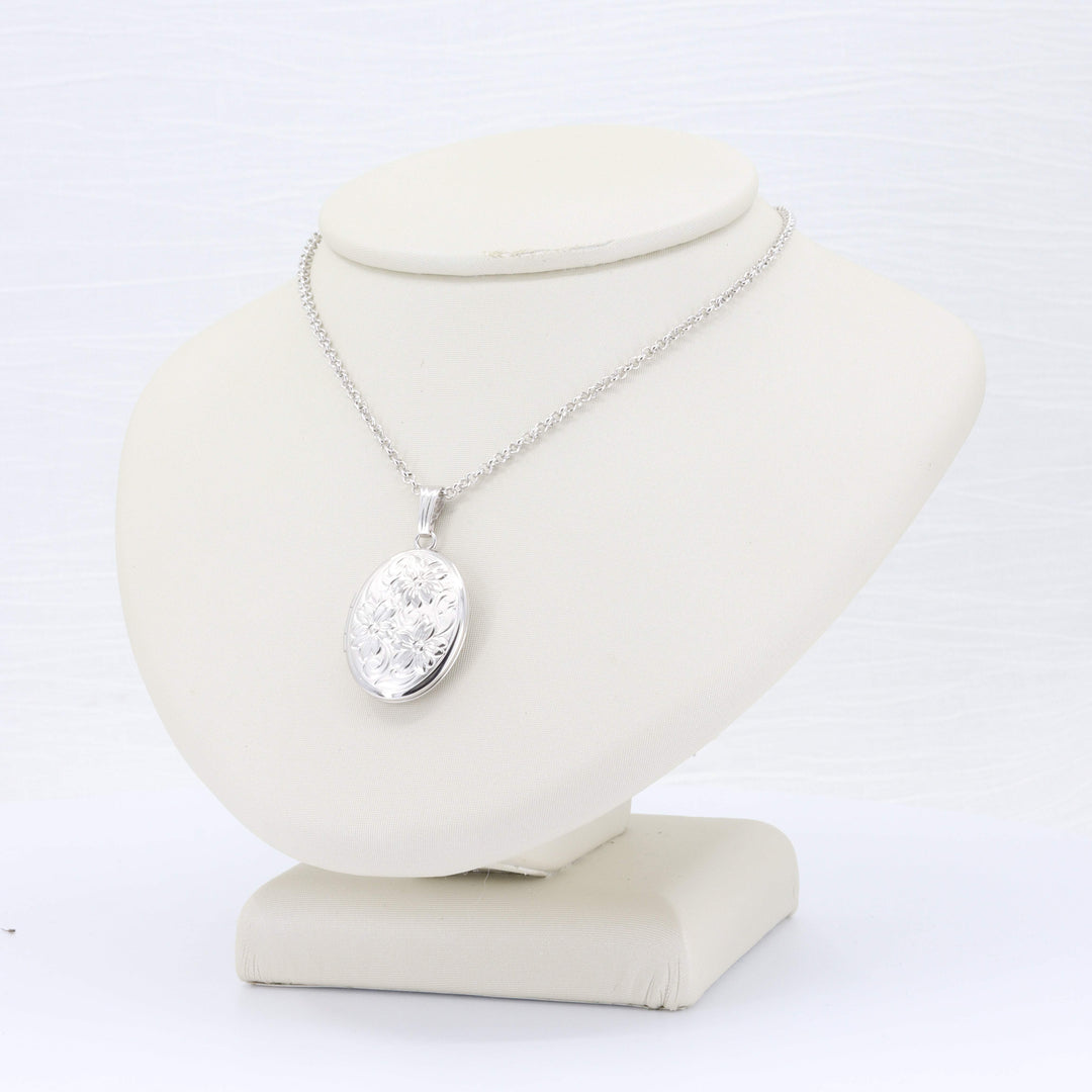 Silver floral locket pendant necklace on a sleek display stand, featuring intricate detailing and a sparkling chain.