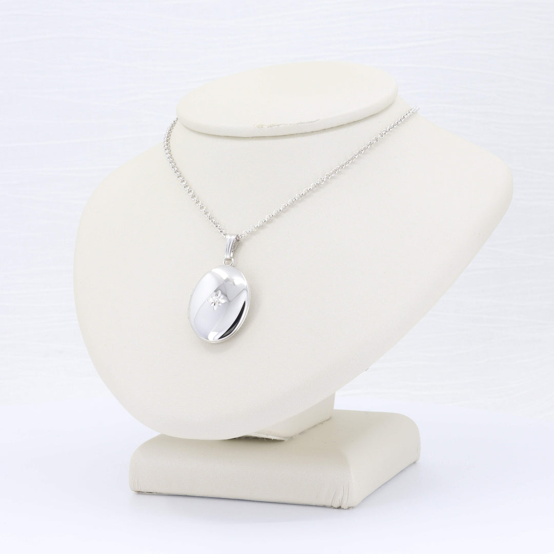 Silver oval pendant necklace with a delicate chain, featuring a subtle diamond accent on a display stand.