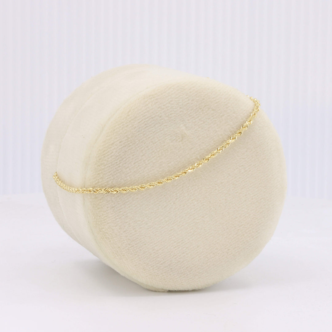 Cream fabric display with a delicate gold braided chain bracelet, showcasing elegant style for jewelry enthusiasts.