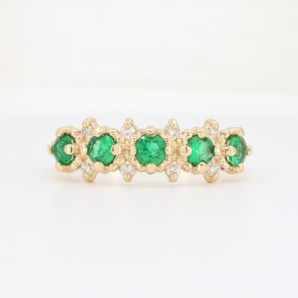 Gold eternity band ring featuring emerald gemstones and sparkling white diamonds. Elegant and luxurious design.
