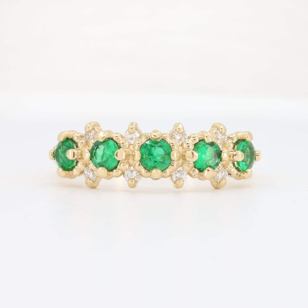 Gold eternity band ring featuring emerald gemstones and sparkling white diamonds. Elegant and luxurious design.