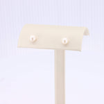 Load image into Gallery viewer, Elegant white pearl stud earrings displayed on a soft beige stand, perfect for any occasion.