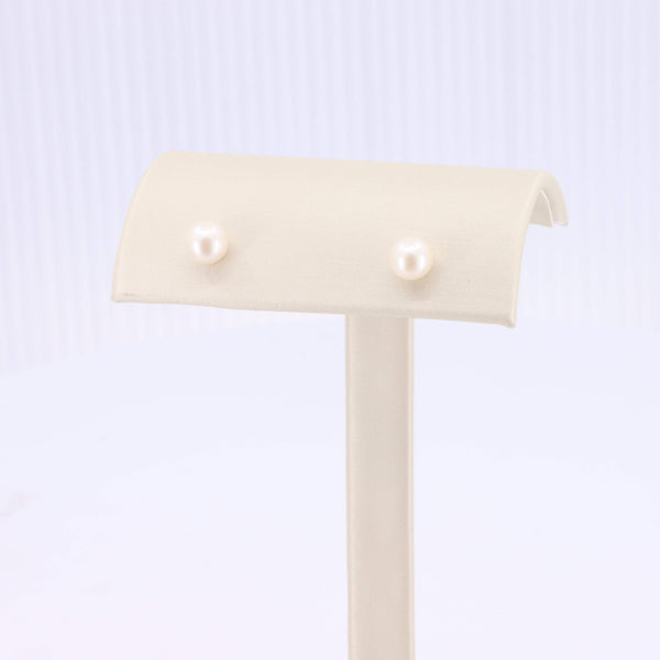 Elegant white pearl stud earrings displayed on a soft beige stand, perfect for any occasion.