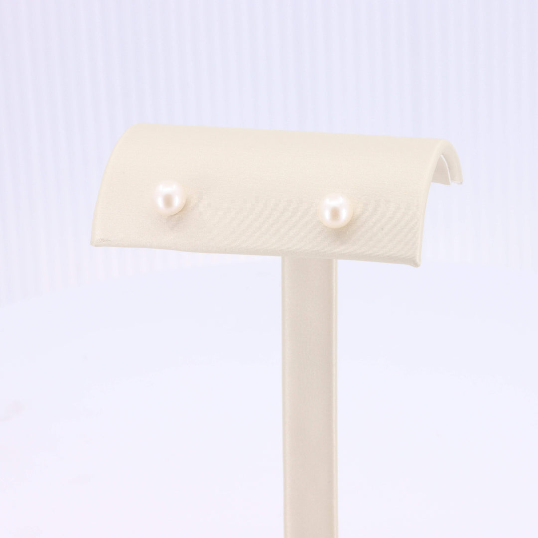 Elegant white pearl stud earrings displayed on a soft beige stand, perfect for any occasion.