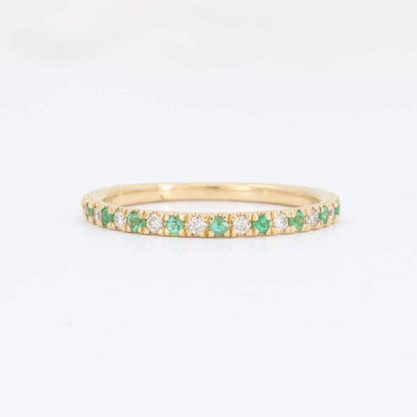 Gold eternity band ring with emerald and diamond accents, featuring a sleek, modern design.