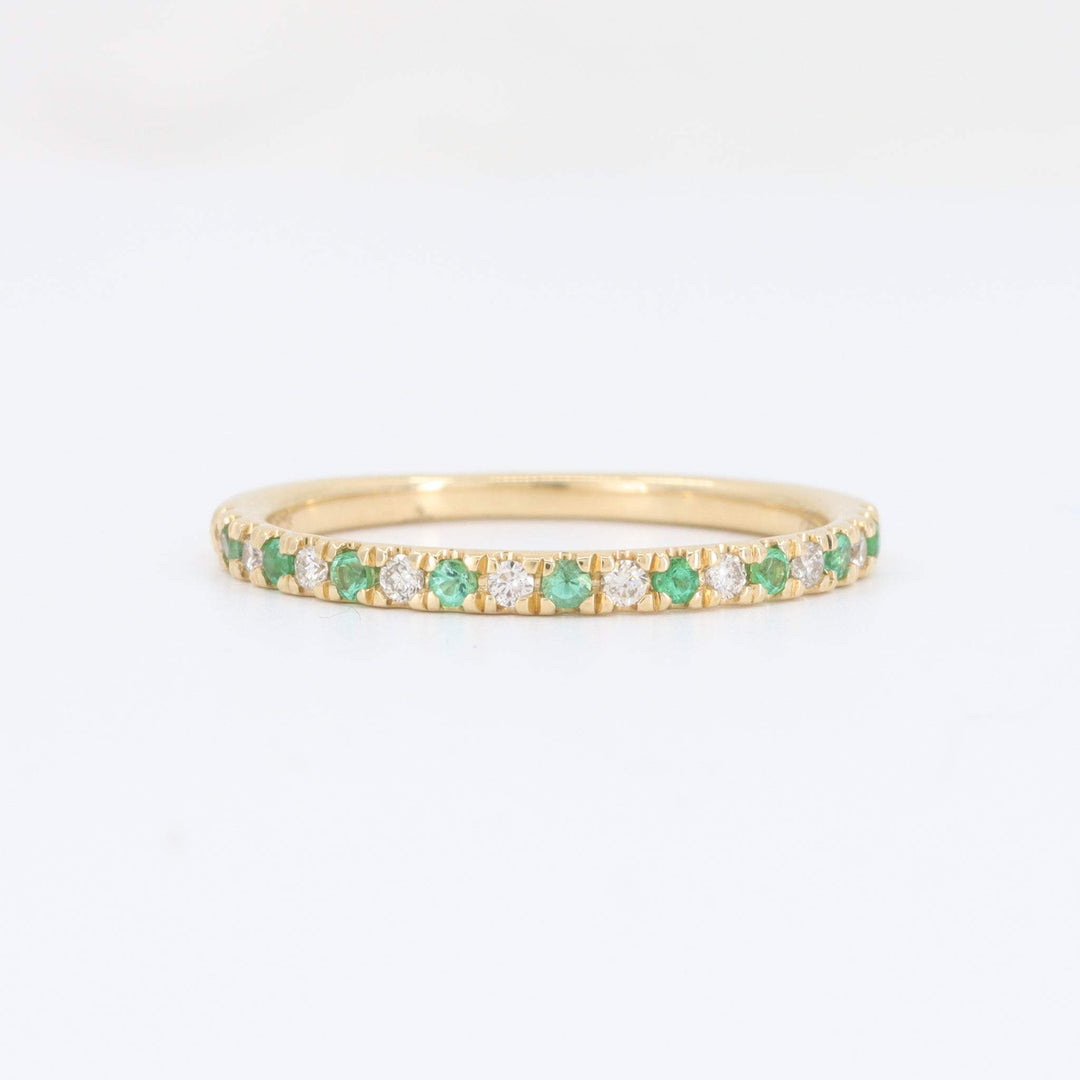 Gold eternity band ring with emerald and diamond accents, featuring a sleek, modern design.