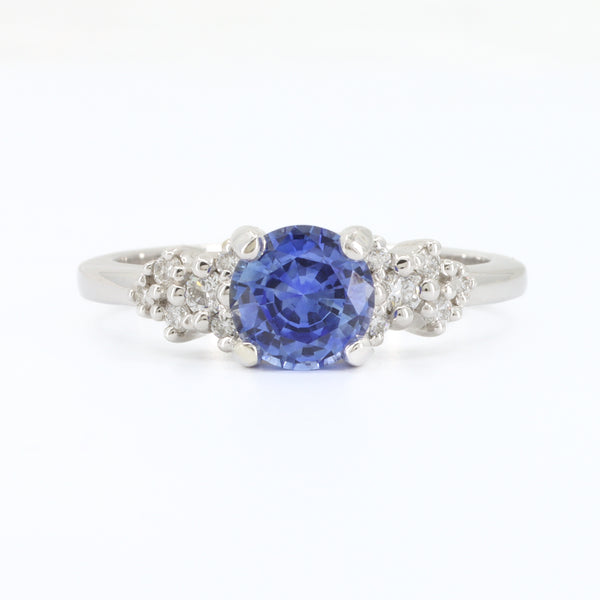 Sapphire and diamond ring in white gold, featuring a round blue sapphire center and floral diamond accents.