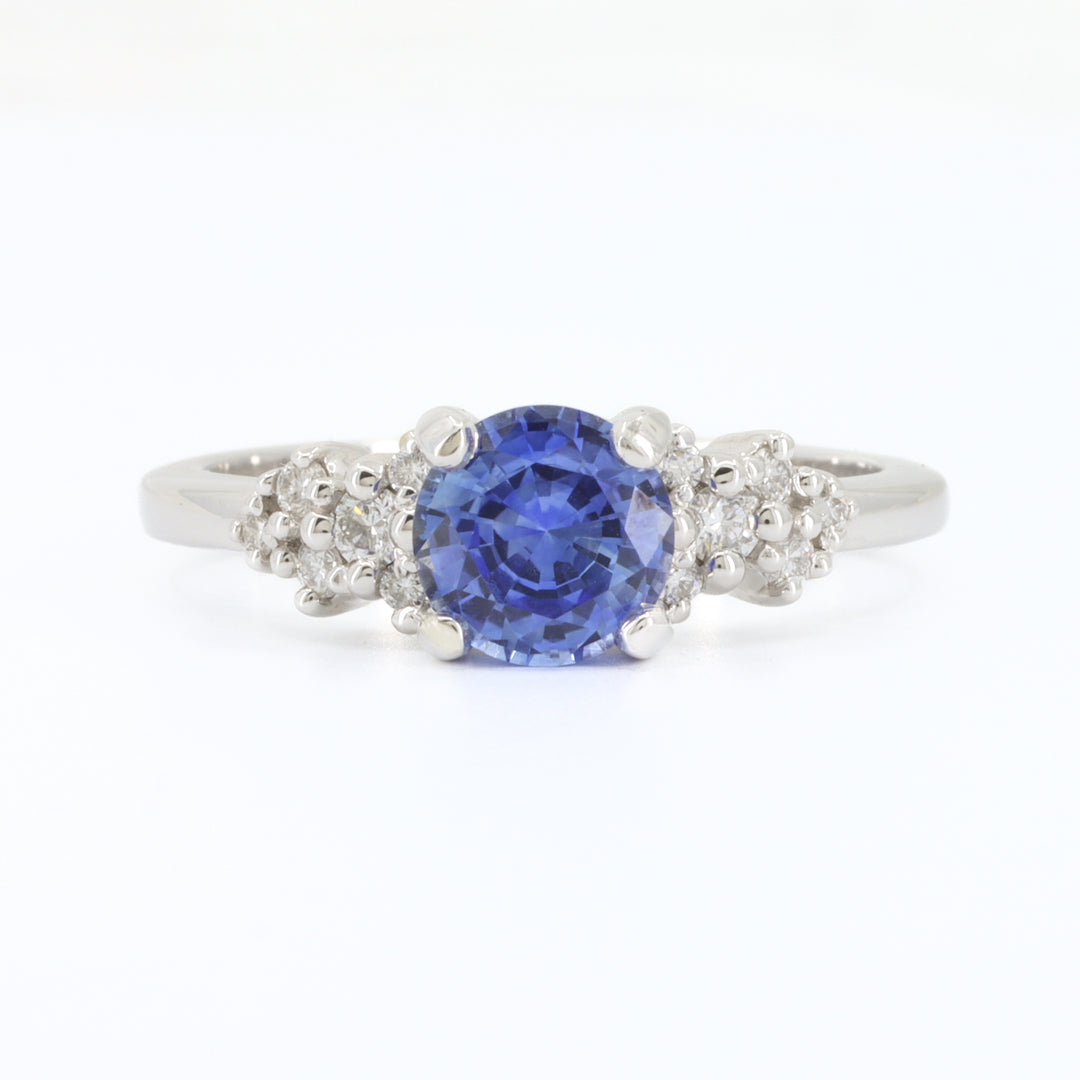 Sapphire and diamond ring in white gold, featuring a round blue sapphire center and floral diamond accents.