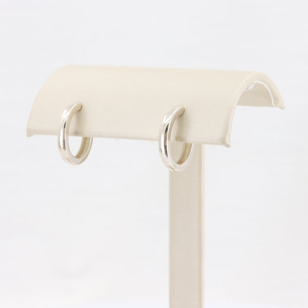 Silver hoop earrings displayed on a beige jewelry stand, featuring a sleek, polished finish.