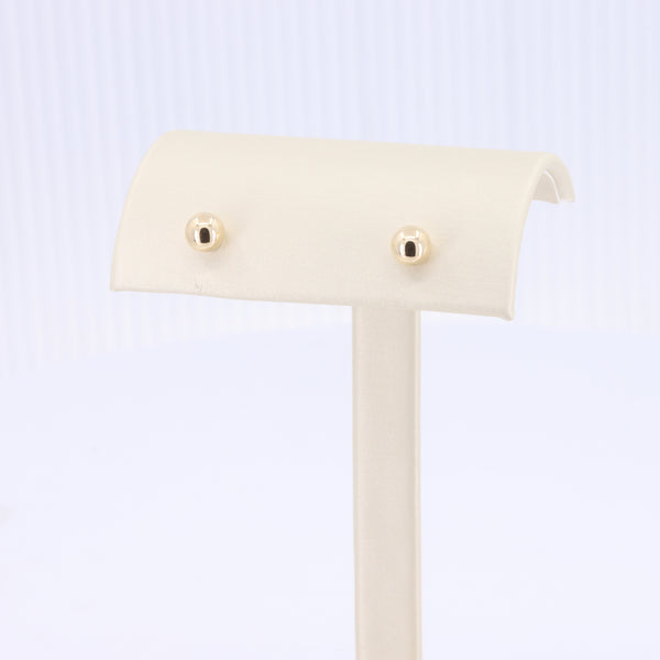 Gold stud earrings featuring a classic, minimalist design on a cream display stand.