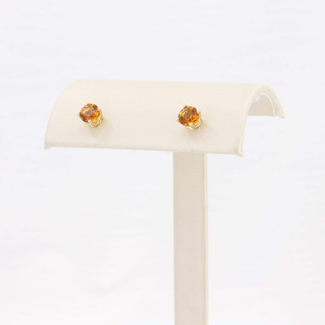 Gold stud earrings with amber-colored crystals on a cream display stand. Elegant and versatile for any occasion.