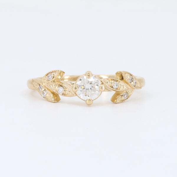 Gold leaf engagement ring with a center diamond and accent stones, featuring intricate vintage-inspired design.