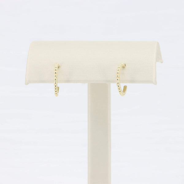 Gold-tone hoop earrings with a textured design displayed on a soft fabric stand. Ideal for everyday wear.