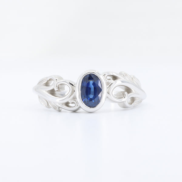 Sterling silver ring with an oval blue sapphire and intricate swirl design, perfect for elegant occasions.